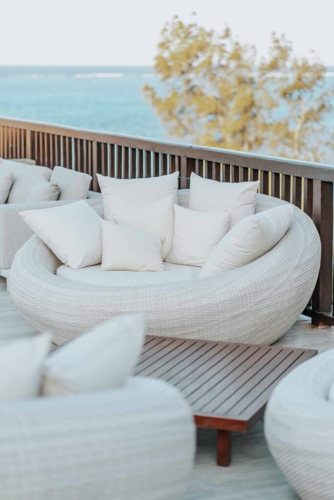 Chic outdoor seating area with stylish white sofas and pillows by the sea, perfect for relaxation.