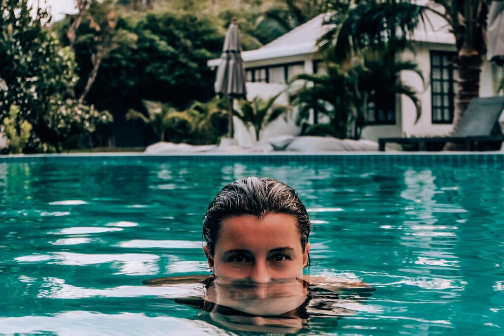 Woman peacefully swimming in a luxurious outdoor pool surrounded by lush greenery.